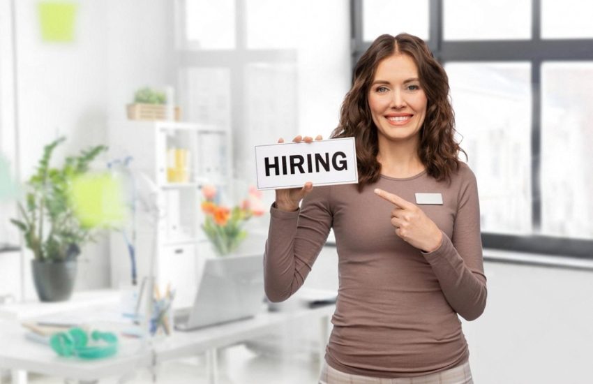 Smiling HR specialist in a bright office holding a Hiring sign, representing manager recruitment in the UAE